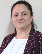 Silvana Garcia Andre é uma mulher branca, com cabelos compridos lisos presos com rabo de cavalo. Usa camisa branca e casaco bordô.