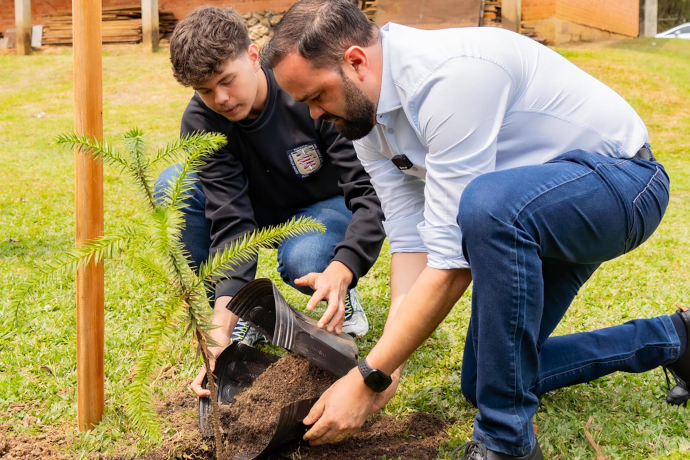 Foto secretário Roni Miranda plantando árvore junto com um estudante