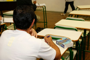 Adulto sentado à carteira, de costas, escrevendo