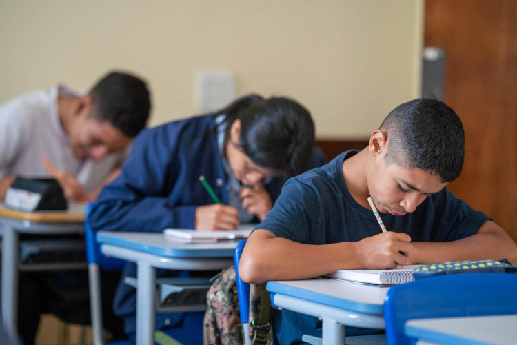 Foto contendo 3 estudantes em sala de aula.