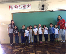 Ana Laura, do 2° ano do ensino, dá aulas de inglês para alunos das séries iniciais do ensino fundamental nas escolas municipais da sua cidade uma vez por semana há dois anos e meio