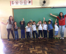 Ana Laura, do 2° ano do ensino, dá aulas de inglês para alunos das séries iniciais do ensino fundamental nas escolas municipais da sua cidade uma vez por semana há dois anos e meio