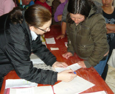Direção e equipe pedagógica entregam boletins aos pais em salão de bairro do município, aproximando escola e família de alunos.