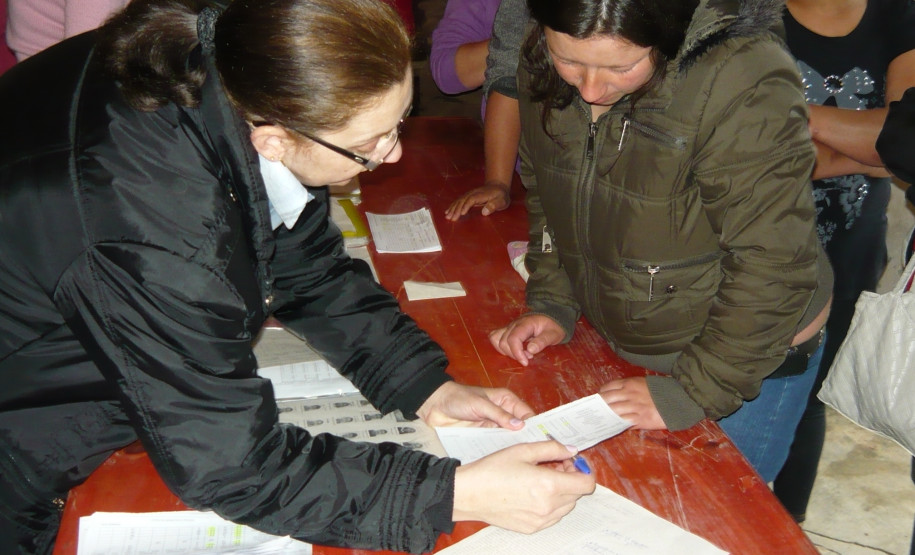 Direção e equipe pedagógica entregam boletins aos pais em salão de bairro do município, aproximando escola e família de alunos.