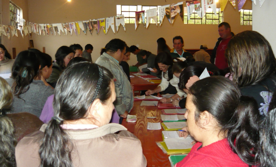 Direção e equipe pedagógica entregam boletins aos pais em salão de bairro do município, aproximando escola e família de alunos.